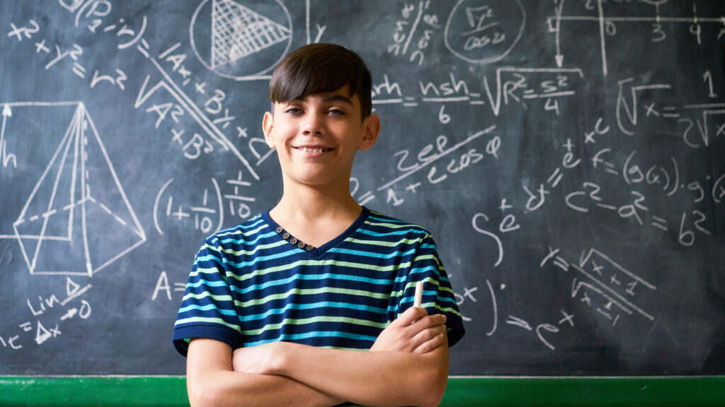 Niño en frente de una pizarra con fórmulas matemáticas